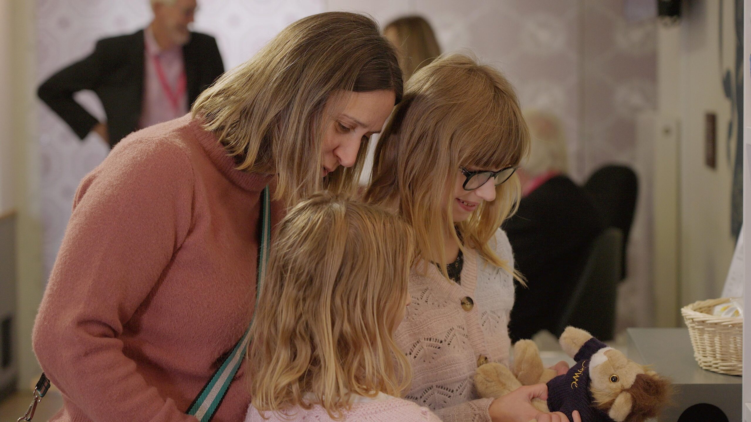 A mum in her thirties looks at souvenirs with two young girls in the shop at Stowe House. The young girl holds a cuddly lion.